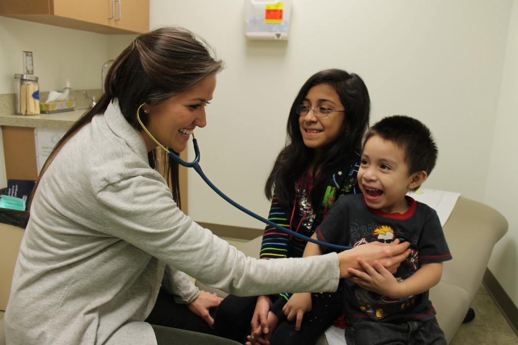 JCCHC pediatric nurse practitioner Kyli Riehl, left, checks 3-year-old Brian Salinas s his sister, Alondra, looks on.
