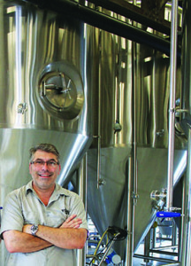 Yee-Haw brewmaster Brandon Greenwood in front of two of the facility’s 20 brewing tanks. Photos by Jeff Keeling