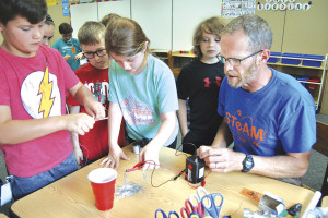 Rob Johnson (right) looks on as a STEAM camper uses her electromagnet to pick up paperclips and deposit them into a cup.